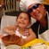 A man in an apron and chefs toque smiles alongside a young girl making salsa